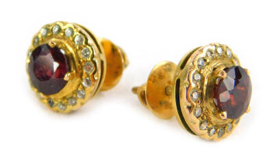 A pair of ruby and diamond earrings, each with round brilliant cut ruby surrounded by tiny diamonds, with screw on backs, yellow metal, unmarked, 4g all in.