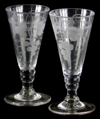 A pair of late 18th/early 19thC glass ale flutes, with engraved decoration of grapes, wheat, etc., with a tapering bowl and a domed foot, 14cm high.