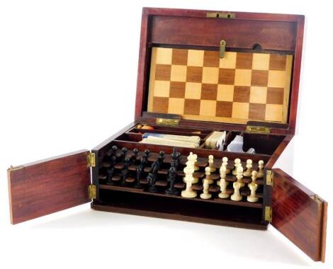 A late 19th/early 20thC games compendium, comprising chess board, bone chess pieces, Bakelite draughts and other items to include playing cards, etc., in stained beech cabinet, 28cm wide.