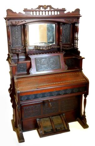 A late 19thC Canadian walnut harmonium, the elaborate raised back with a central bevelled mirror plate, flanked by carved panels, turned pillars and galleries, the base with simulated ivory keys, stamped Bell Guelph Ontario Canada, 198cm high, 127cm wide