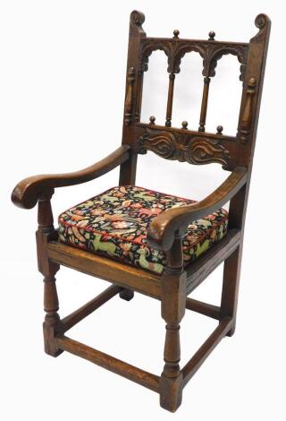 An oak throne type chair in 17thC style, the back with spindle turned and leaf carved arches, above a leaf carved cartouche, with shaped arms, solid seat on turned legs.