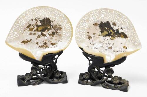 A pair of Chinese pierced and carved mother of pearl shells, decorated in lacquer with birds and flowers, on carved hardwood stands, 19thC, 27.5cm high.