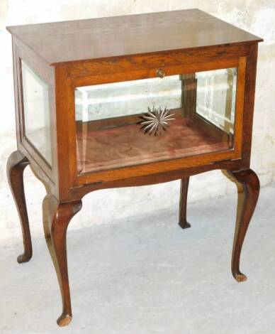An early 20thC oak display cabinet, of rectangular form with four bevel glass panels and hinged front, revealing a plain interior on cabriole legs, terminating in pad feet, 75cm high, 58cm wide, 38cm deep. (AF)