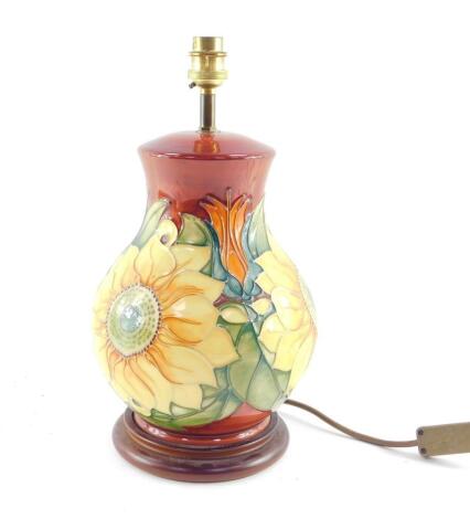 A Moorcroft pottery table lamp decorated in the Inca Sunflower pattern, of baluster form, against a red ground, 35cm high.
