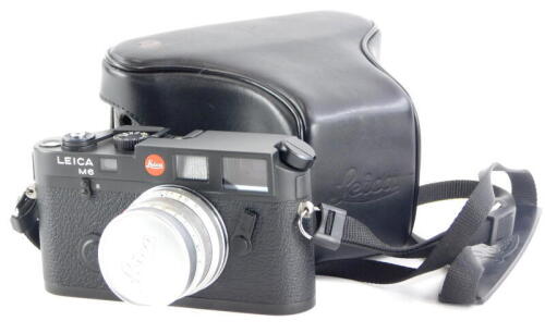 A black Leica M6 camera, with a Leitz 35mm f wide angle Summicron lens, number 1745070, in a leather case.