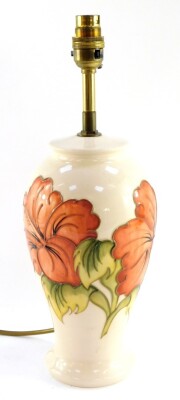 In Display cabinet A Moorcroft pottery table lamp decorated in the Hibiscus pattern, of baluster form, decorated against a cream ground, impressed marks, 38cm high.