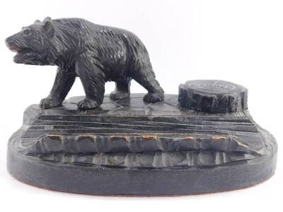 A Black Forest late 19thC desk stand, carved with a bear and a tree stump hinge lidded inkwell, on a naturalistic oval base, 24cm wide.