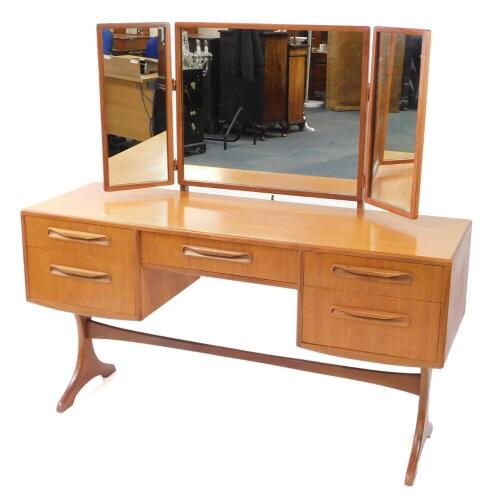 A G plan teak dressing table, with a tryptic mirror back, over a central fitted jewellery drawer, flanked by four further drawers, raised on X shaped end supports united by a single stretcher, 131.5cm high, 137cm wide, 46cm deep.