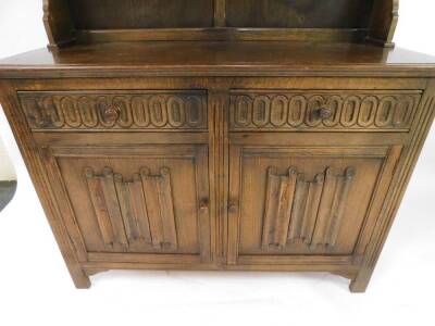 An oak dresser, the out swept pediment above a two shelf plate rack, over two frieze drawers above linenfold panelled doors, raised on channel square legs, 182.5cm high, 127 cm wide, 38cm deep. - 2