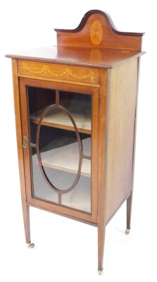 An Edwardian mahogany and inlaid display cabinet, the domed back with paterae inlay, over a glazed door enclosing two shelves, raised on tapering square legs, brass capped on castors, 122cm high, 50.5cm wide, 41cm deep.