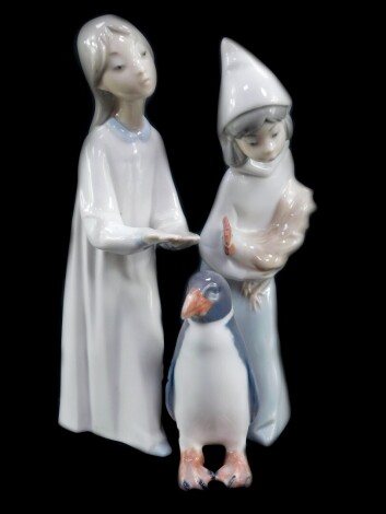 A Royal Copenhagen porcelain figure modelled as a penguin, no 1283., printed and painted marks, together with a Lladro porcelain figure of a girl holding a cockerel, and a further Lladro figure of a girl extending her hands. (AF). (3)