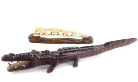 An Indian early 20thC tusk ivory carving of a line of graduated elephants, in a hardwood stand, 29.5cm wide (AF), together with a hardwood carved figure of an alligator, 48cm wide. (2)