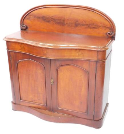 A Victorian flame mahogany serpentine chiffonier, the curved foliate scroll back over a cushion drawer above a pair of panelled doors raised on a plinth base over bun feet, 120.5cm high, 113.5cm wide, 54cm deep.