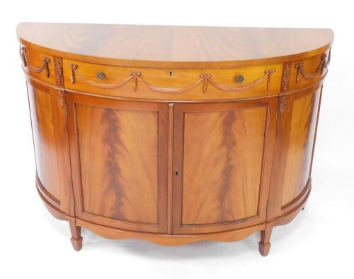 An Adam style reproduction demi lune commode, with a single frieze drawer over a pair of cupboard doors, raised on tapering square legs on spade feet, 88cm high, 131cm wide, 50cm deep.