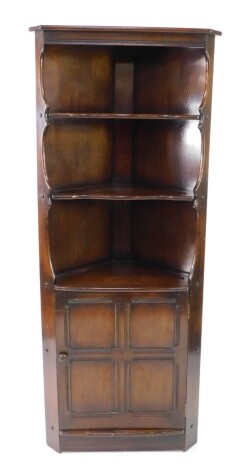 An Ercol dark elm corner display cabinet, the outswept pediment over two shaped shelves above a panelled cupboard door, raised on a plinth base, 184cm high, 75cm wide, 42cm deep.