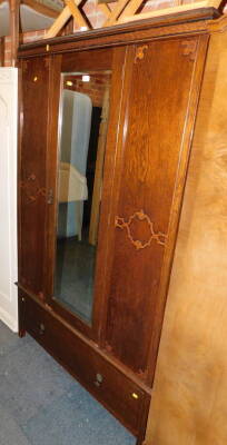 An early 20thC oak and oak veneered wardrobe, with central mirrored door above single drawer, 189cm high, 118cm wide, 60cm deep.