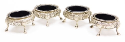 A set of four Victorian silver salts, with blue glass liners, having chased rim with repousse floral and cartouche sides, on four shell knee stepped feet. Maker Daniel & John Welby. London 1878, 12oz.