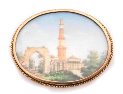 A late 19thC painted porcelain oval brooch, with a scene of The Qutub Minar in Delhi, in a yellow metal oval frame, with rope twist border, on single pin back with pendant loop, stamped 9ct, 5.5cm wide, 20.5g all in.