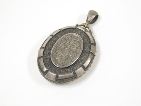 A Victorian locket, oval with embossed and engraved decoration of flowers, in a white metal setting, unmarked, 5cm high, 16.5g all in.