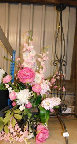 A cast metal altar flower stand, with floral artificial flower display of various pink flowers on a blackened metal tripod stand base.