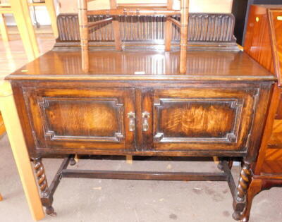 An oak Old Charm console table, the high shield carved back, above two cupboard doors on barleytwist column legs, 110cm high, 106cm wide, 48cm deep.