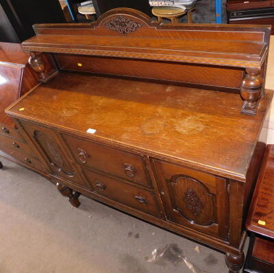 A carved oak sideboard, the shield shaped top with scroll applied decoration on baluster columns, above two central drawers with two cupboard doors, similar finial decoration applied on baluster legs, 132cm high, 119cm wide, 46cm deep. (AF)