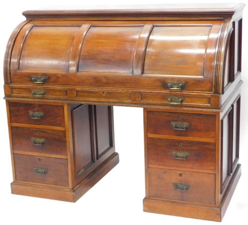 A late Victorian walnut cylinder desk, with a moulded top and a triple panelled fall, enclosing a fitted interior with red leather insets, pigeon holes and drawers, each with teardrop handles above six drawers, each with engraved brass drop handles, on a