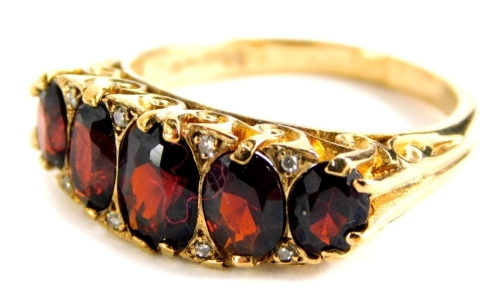 A 9ct gold garnet set gypsy ring, with five garnets and tiny diamond set shoulders, in a raised claw setting, with scroll design shoulders, ring size O, 4.9g all in, boxed.