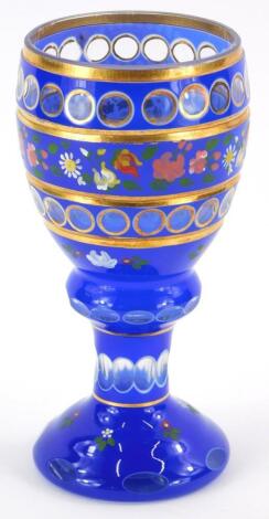 A Bohemian style blue flash glass goblet, with gilt decoration and bands of flowers in coloured enamels, 18.5cm high.