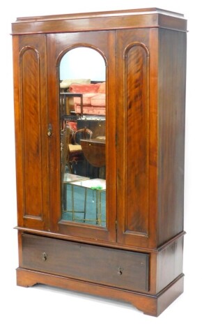 An early 20thC mahogany and satin walnut wardrobe, with a moulded cornice above a single mirrored door, flanked by arched panels above a frieze drawer on bracket feet, 199cm high, 115cm wide.