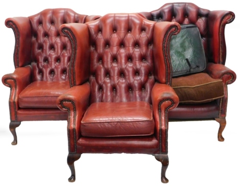 Three similar red studded leather Chesterfield type wing back chairs in 18thC style, each on cabriole legs. (AF) The upholstery in this lot does not comply with the 1988 (Fire & Fire Furnishing) Regulations, unless sold to a known exporter or upholsterer 