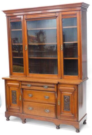 A late 19th/early 20thC walnut bookcase, the top with a moulded cornice with three glazed doors enclosing adjustable shelves, the breakfront base with a frieze drawer above two further drawers, flanked by two carved panel doors on bun feet, 228cm high, 1