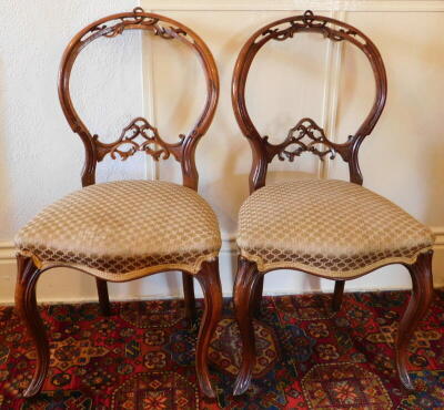 A pair of Victorian walnut cameo back dining chairs, with pierced frames over stuffed seats and cabriole legs.