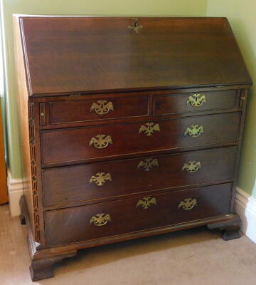 A George III oak bureau, with fall flap revealing a fitted interior, resting on lopers, three short and three long graduated drawers, with brass solid back plate handles and ogee bracket feet, 107cm wide.