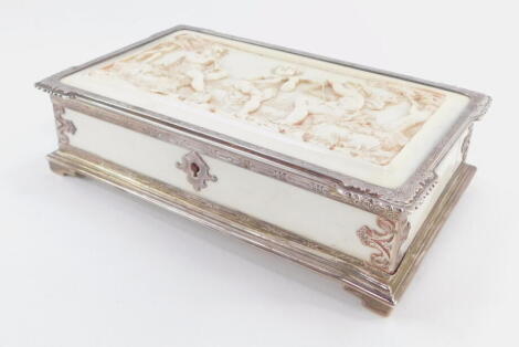 A Victorian silver and ivory box, of rectangular form, the lid heavily carved with three cherubs playing musical instruments in a forest setting, with silver mounts, elaborate escutcheon and bracket feet, London 1899, 5cm high, 18cm wide, 10cm deep.