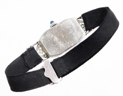 An early 20thC diamond set ladies cocktail watch, with a hexagonal shaped dial, in a white enamel finish, with cabochon sapphire dial, in a white metal casing stamped platinum, on a black ribbon band, the watch head 2.5cm long, in a Pearce & Sons Ltd of L - 3