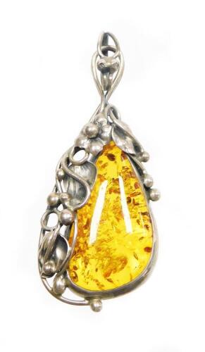 A silver and amber pendant, the pear cut amber stone, surrounded by vines of flowers and leaves, in white metal, unmarked, with pendant clasp, 6cm high, 10g all in.