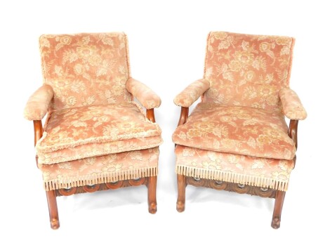 A pair of French early 20thC walnut stained armchairs, each with bolster backs and seats and removable cushions, on serpentine front legs and sabre back legs, plain stretchers, 94cm high.