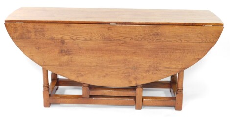 A 17thC style oak drop leaf gate leg table, the round plank top raised on turned baluster columns joined by heavy block stretchers, the whole terminating in block feet, 77cm high, 152cm wide, 168cm deep.