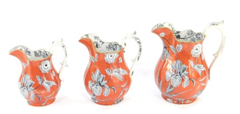 A graduated set of three 19thC transfer printed jugs, each decorated with flowers in black on an orange ground, with moulded handles, on circular feet, each numbered 1791, the largest 22cm high. (3)