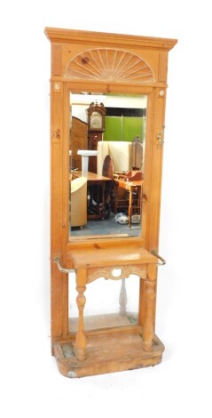 An early 20thC pine hall stand, the fixed moulded cornice raised above a sun moulding, with bevel glass flanked by roundels and hooks, the fixed centre flanked by umbrella compartment and D-end base with back block stiles, 210cm high, 76cm wide, 42cm deep