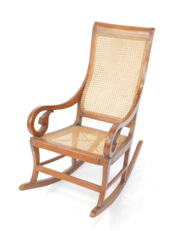 An early 20thC Bergere rocking chair, with cane work back and seat, heavily carved scroll arms and front plain horizontal stretcher on a rocker base, 104cm high.