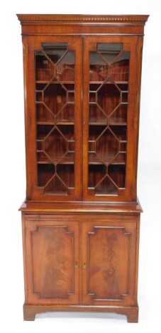 A Georgian style mahogany cupboard bookcase, the dentil moulded pediment over a pair of astragal glazed doors, enclosing three shelves, above a brushing slide and pair of cupboard doors, enclosing two small shelves, raised on bracket feet, 191.5cm high, 7