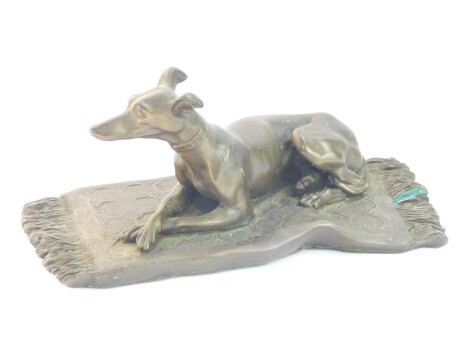 A bronzed plaster figure of a greyhound, modelled recumbent on a rug, stamped OFA, 9.5cm wide. (AF)