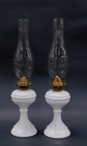 A pair of late 19thC milk glass oil lamps, possibly Sowerby, with moulded fluting and sea serpents, with chimneys, 48cm high.