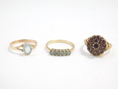 A 9ct gold and aquamarine solitaire ring, size R, 9ct gold and garnet cluster ring, size Q/R, and a further six stone gem set ring, in yellow metal, size R, 7.2g. (3)