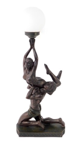 An Art Deco style bronzed figural table lamp, moulding as a kneeling man holding aloft a woman, in turn holding a frosted glass shade, raised on a serpentine base, 78cm high.