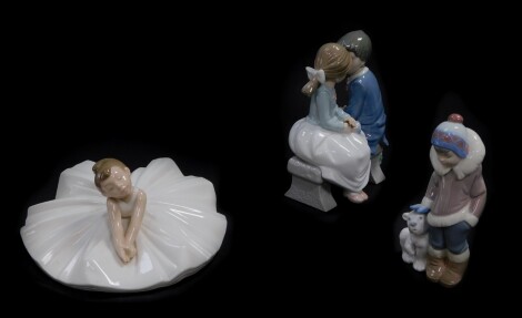A Lladro porcelain figure of an Eskimo boy and polar bear cub, Nao figure group of a boy and girl seated on a bench, both boxed, and a Nao figure of a girl ballerina. (3)