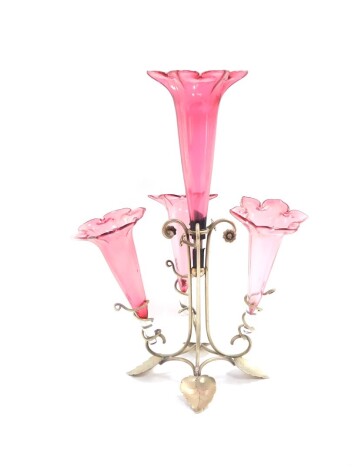 A Victorian silver plate and cranberry glass epergne, with four glass trumpets, raised on a scrolling base with floral and foliate terminals, 35cm high.