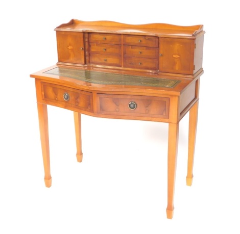 A Sheraton revival Edwardian style yew wood desk, the galleried top raised above six drawers flanked by shell inlaid cupboards, with a tooled leather serpentine subsection set with two further drawers, on square tapering legs terminating in spade feet.